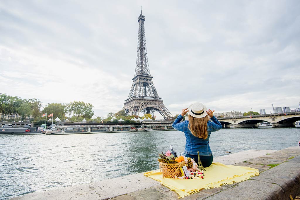 Mulher fazendo piquenique sozinha à beira do rio em Paris. Custo de vida em Paris.