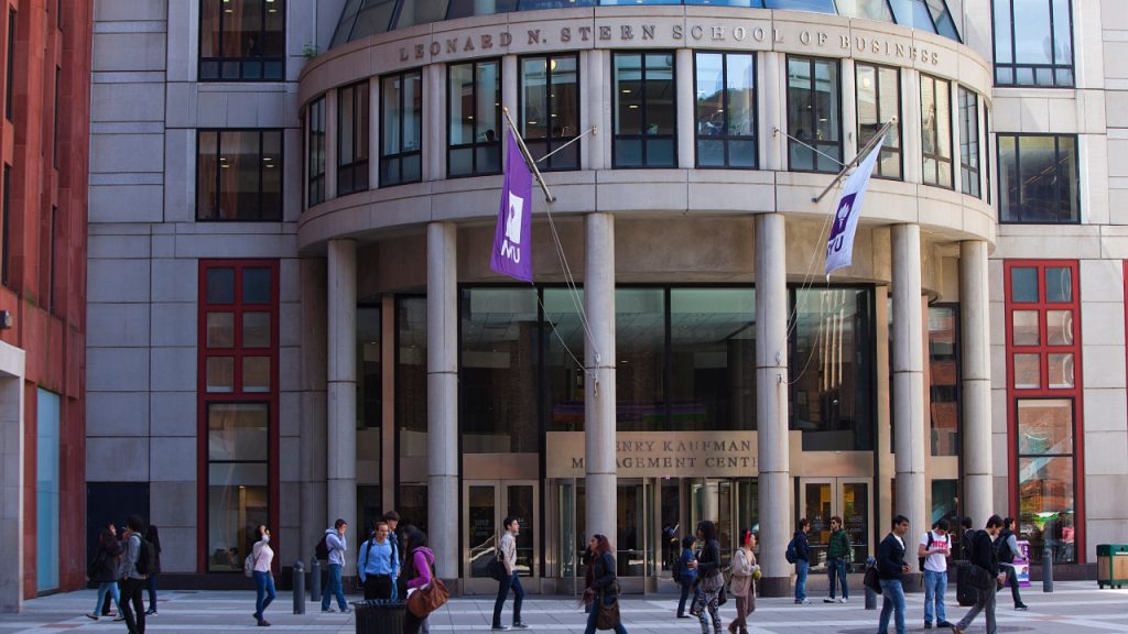Imagem da fachada de um dos prédios da Universidade de Nova York, com bandeiras da logo da instituição penduradas