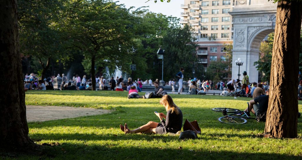Estudante da Universidade de Nova York sentada na grama do campus a mexer no celular