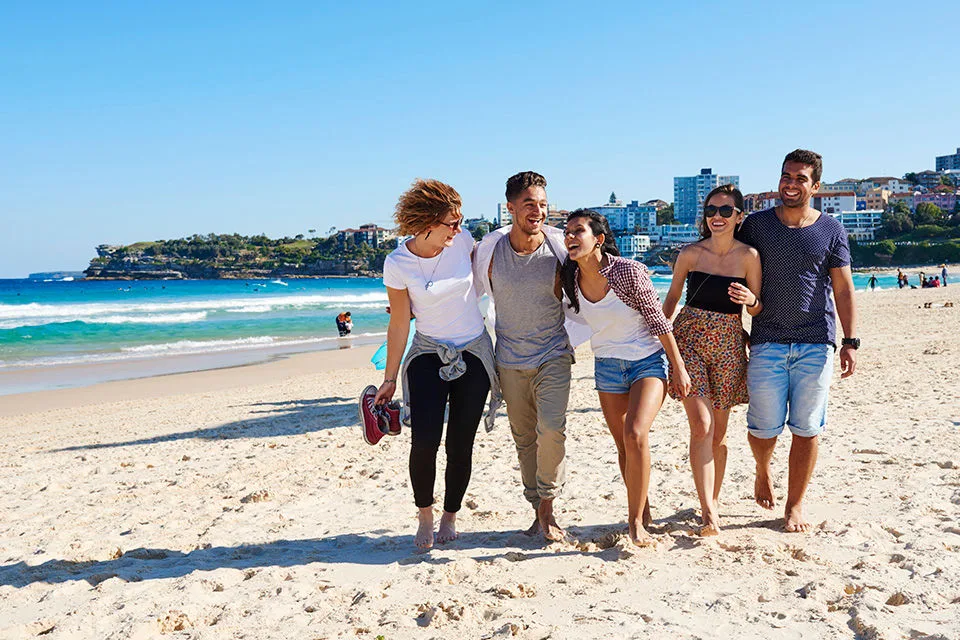 Grupo de amigos caminhando por uma praia na Austrália. Visto de estudo.