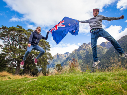 Dois intercambistas segurando a bandeira da Nova Zelândia enquanto pulam