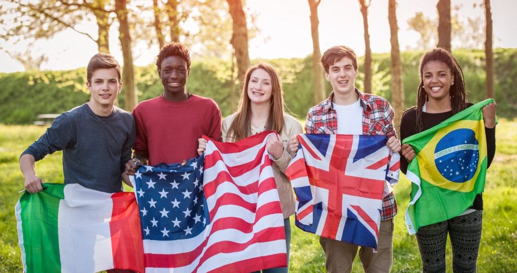 Alunos jovens segurando as bandeiras de seus países: Itália, Estados Unidos, Inglaterra e Brasil.
