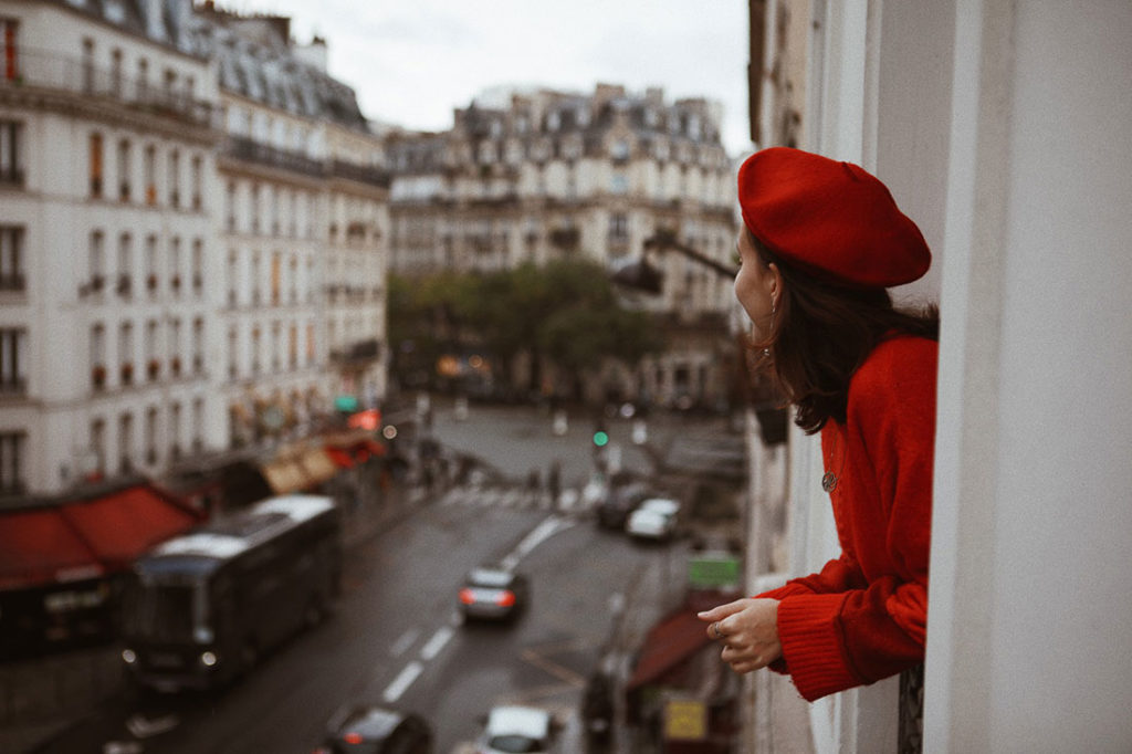 Mulher olhando pela janela de apartamento em Paris